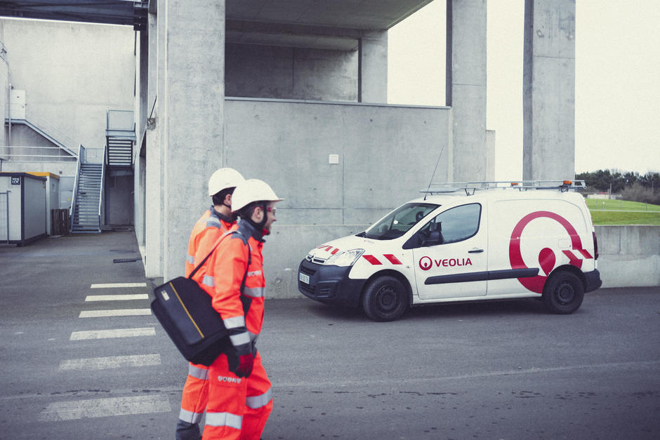 Zwei Veolia Mitarbeiter gehen ins Gelände - dahinter steht ein Veolia Fahrzeug